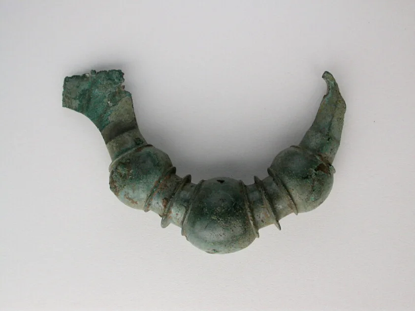 Fíbula de arco antigua en metal oscuro, broche de cierre comparable a los medallones y amuletos que tallaban los azabacheros de Compostela
