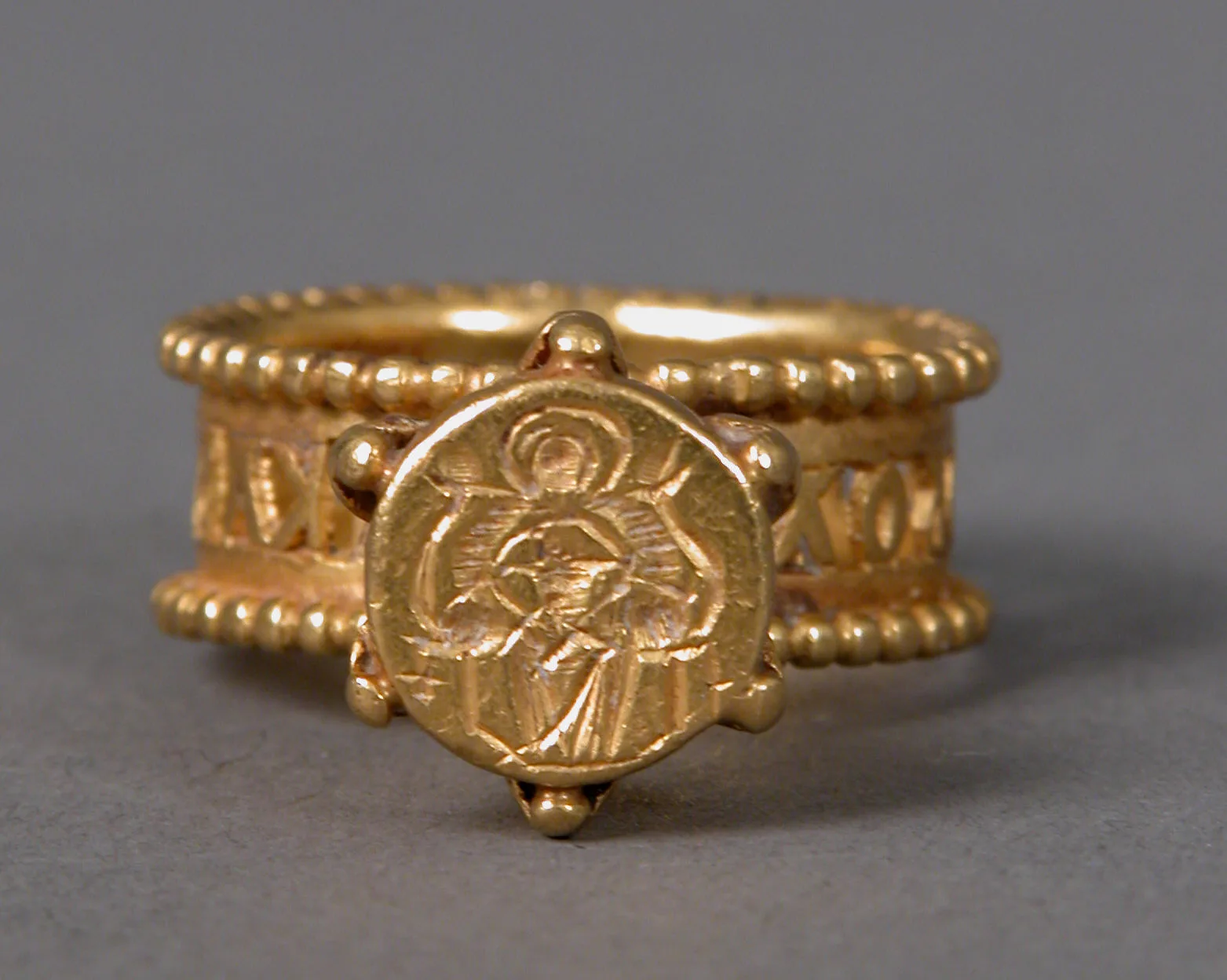 Anillo de oro con una imagen en la cara redonda enmarcada por granulado e inscripción en el aro ancho